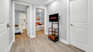 A hallway with a white door, a white wall, and a TV on a stand with the word 'NETFLIX' on it. - *Minutes to BMO Field* 3BR Home in Downtown (Toronto)