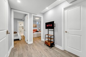 Ein Flur mit einer weißen Tür, einer weißen Wand und einem Fernseher auf einem Schrank mit der Aufschrift 'NETFLIX'.