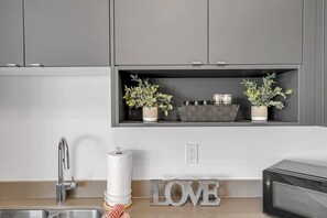 A kitchen with a built-in microwave, a sink with a faucet, and a shelf with potted plants and kitchenware.