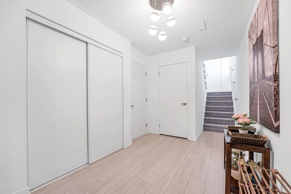 A hallway with a staircase, white doors, and a wall-mounted light fixture.