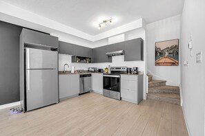A modern kitchen with grey cabinets, stainless steel appliances, and a wooden floor.