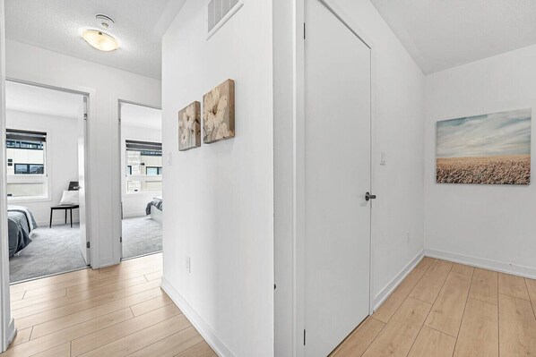 A hallway with a door leading to a bedroom, a living area with a sofa and a table, and a kitchen in the background.