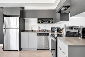 A modern kitchen with stainless steel appliances, grey cabinetry, and a built-in dishwasher.