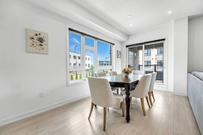 A modern dining area with a large table, six chairs, and a view of the city through large windows.