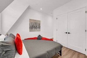 Ein zeitgemäßes Schlafzimmer mit Bett, Kissen, einem Stadtbild und einem Kleiderschrank.