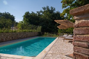 Una piscina con paredes y suelo de piedra, rodeada de árboles y una valla de madera.