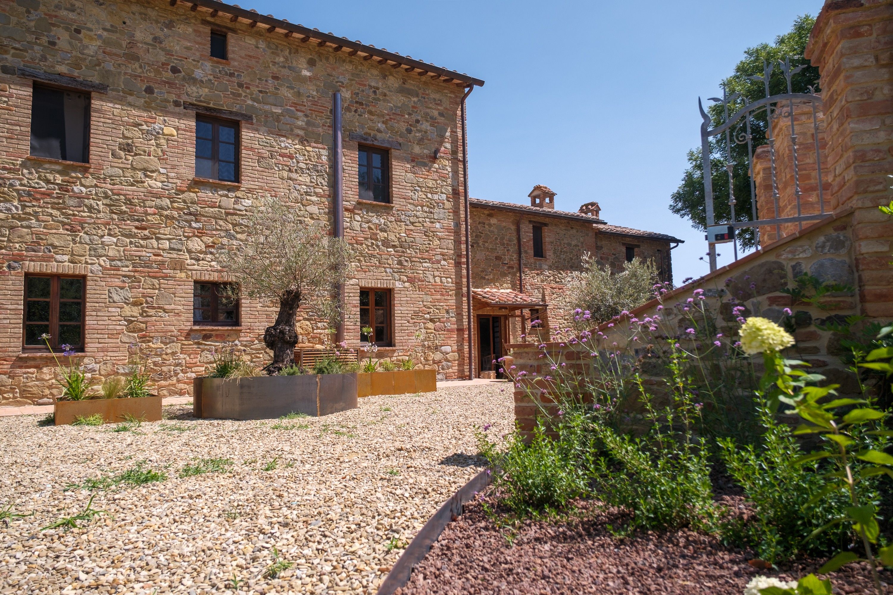 A stone building with multiple windows and a courtyard with gravel and plants.