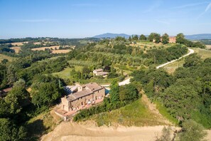Un paisaje rural con una edificación de piedra y techo de tejas, rodeada de exuberante vegetación y un sendero serpenteante.