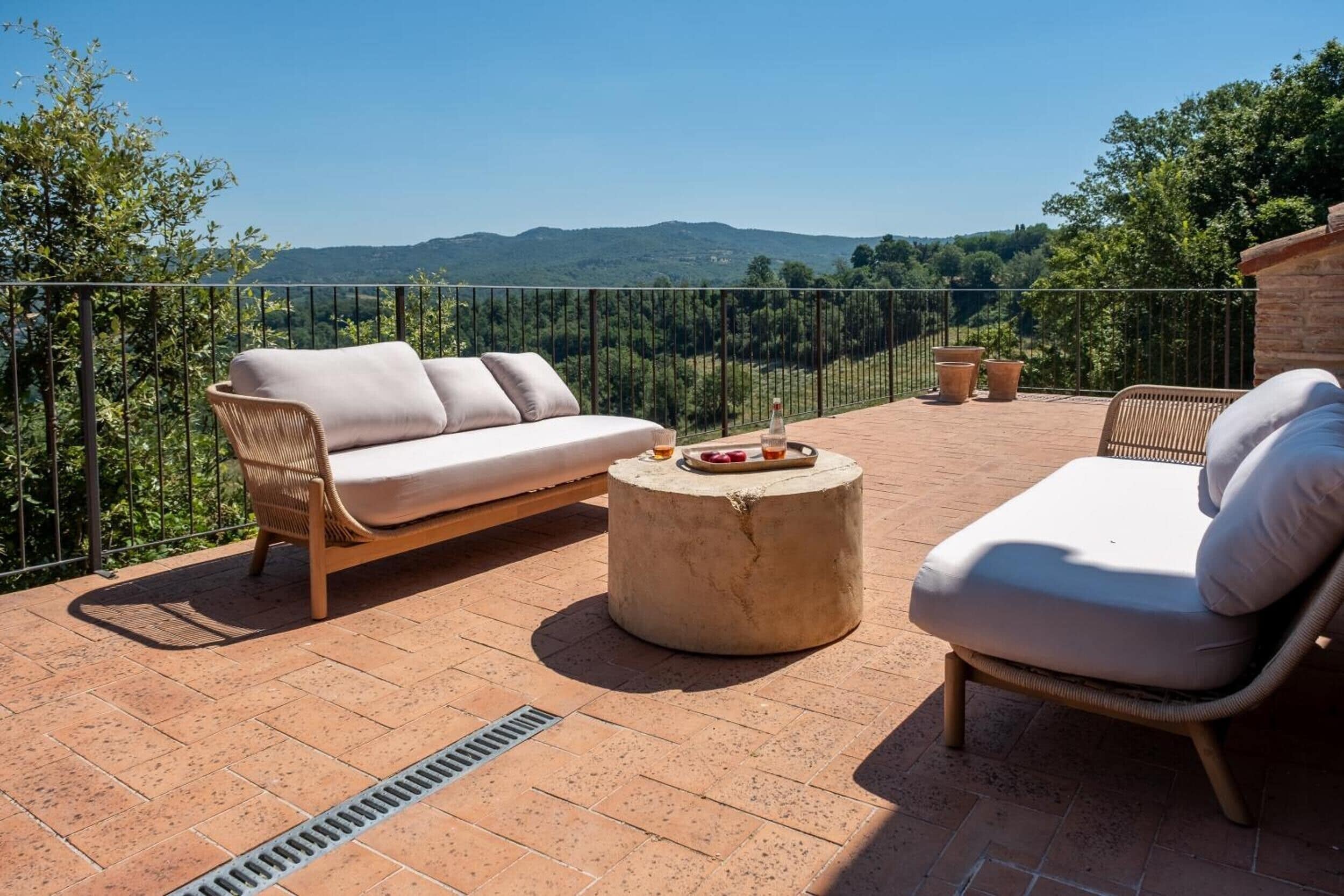 A terrace with a sofa, a chair, and a round table with fruit.