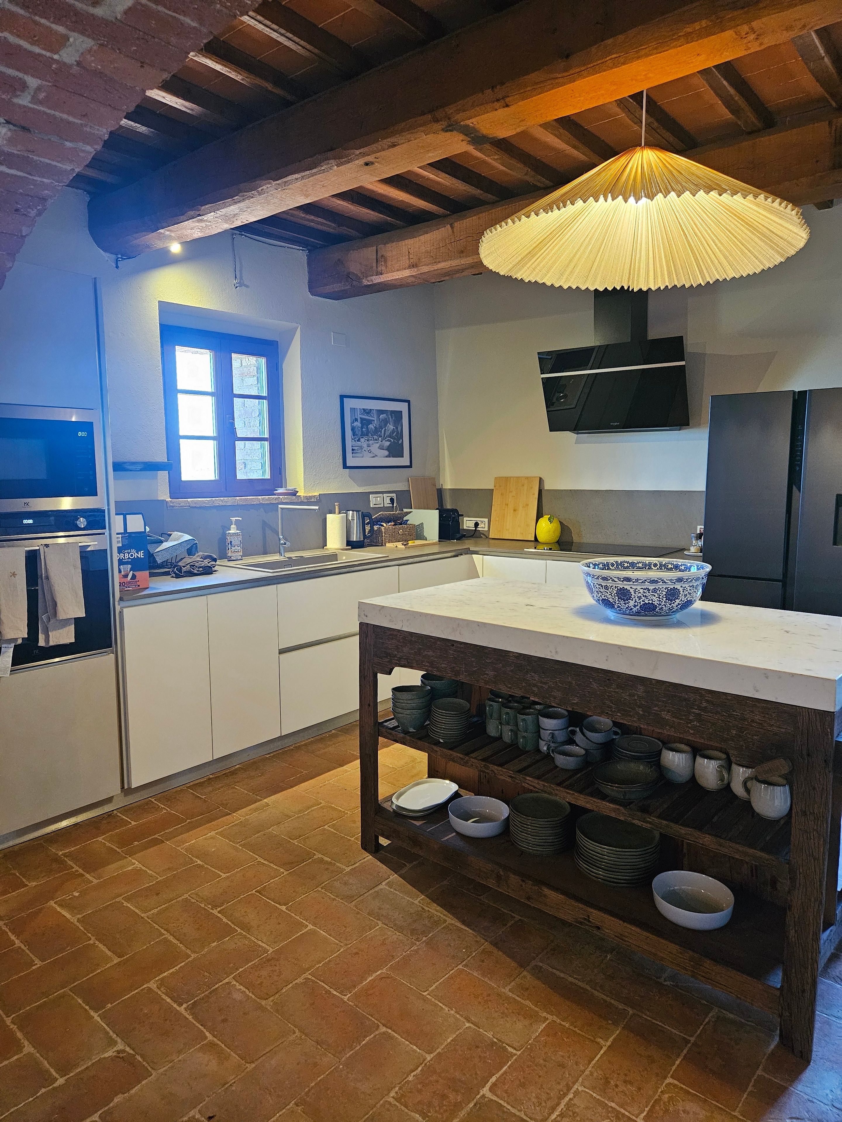 A kitchen with a central island, a hanging light fixture, a window, and a mounted television.