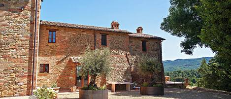 A stone building with a courtyard, outdoor seating, and a view of the hills.