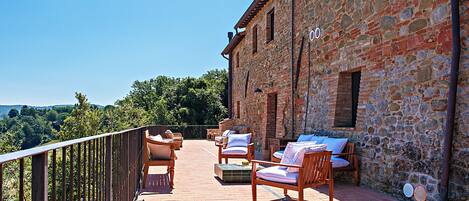 A balcony with outdoor seating and a stone building.