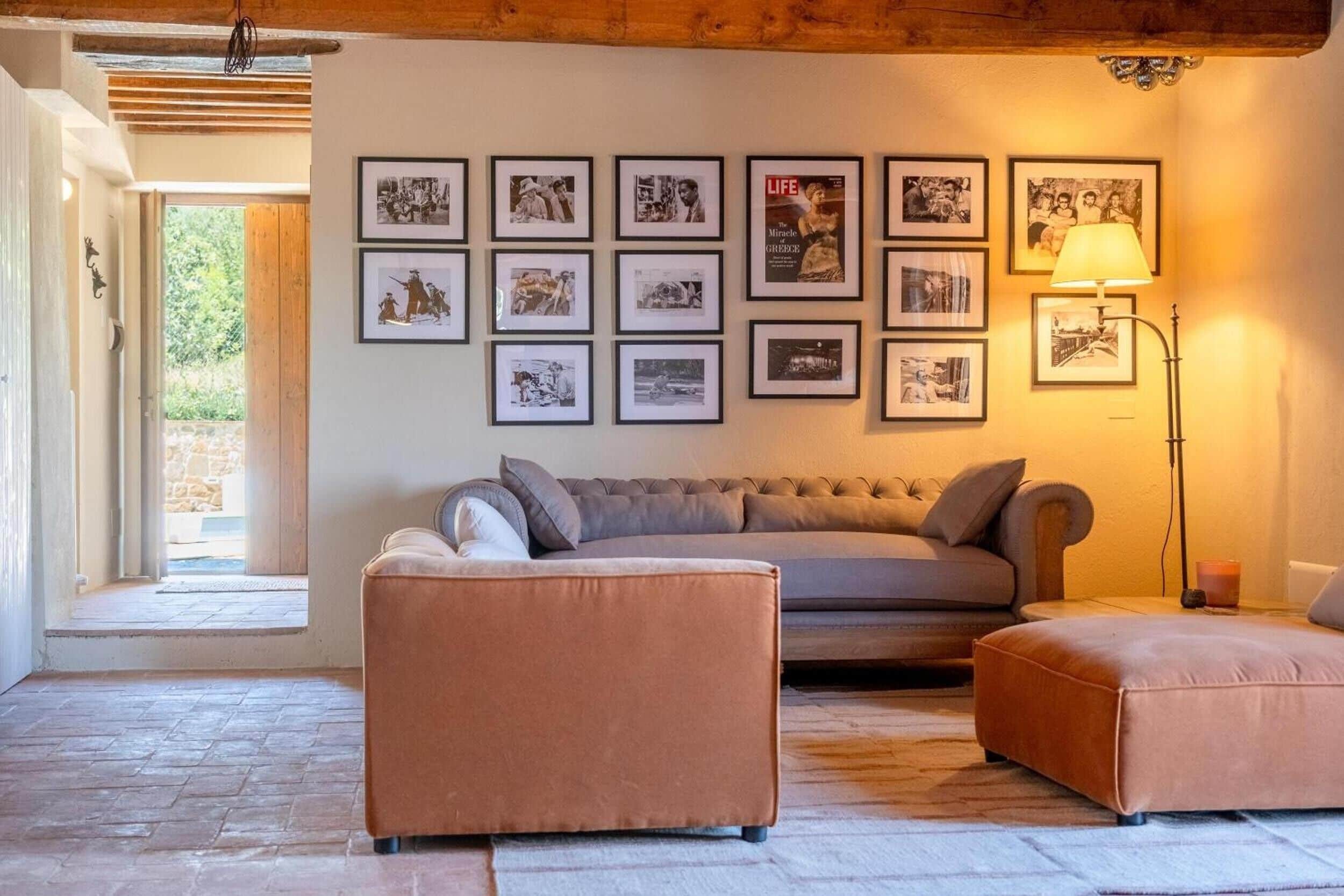 Een woonkamer met een bank, een voetenbankje en ingelijste foto's aan de muur.