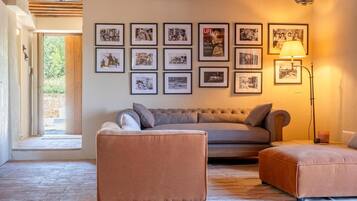 Een woonkamer met een bank, een voetenbankje en ingelijste foto's aan de muur.