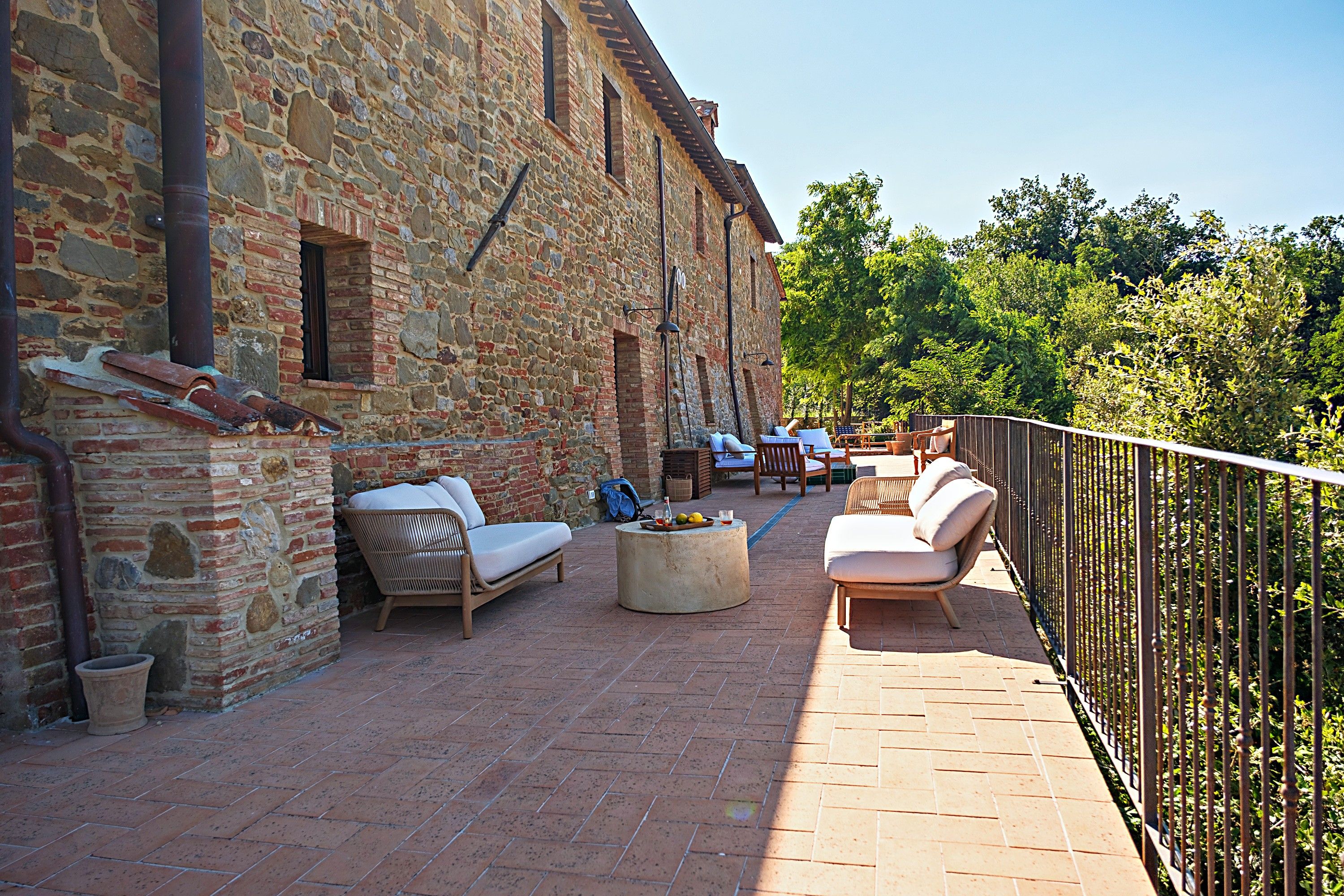 Eine Terrasse im Freien mit Steinmauern, Korbmöbeln und einem Metallgeländer.