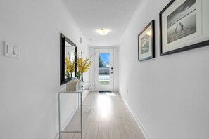 A hallway with a glass console table, framed artwork, and a door leading outside.
