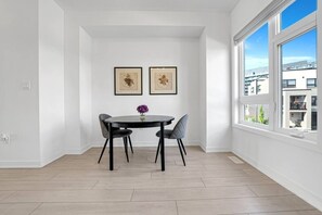 A dining area with a round table, four chairs, and two framed artworks on the wall.