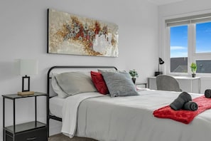 A modern bedroom with a bed, bedside table, lamp, and a large abstract painting.
