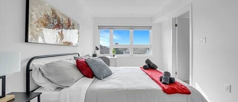 Een moderne slaapkamer met een bed, een bureau, een raam en een schilderij.