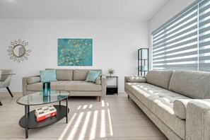 A modern living room with two sofas, a glass coffee table, and a painting on the wall.