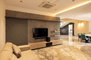 A modern living room with a flat-screen TV, built-in shelves, a sofa, and a dining area with chairs.