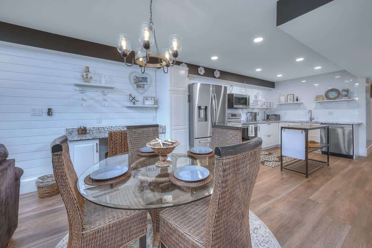 A modern kitchen with white cabinetry, stainless steel appliances, and a dining area with wicker chairs and a glass table.