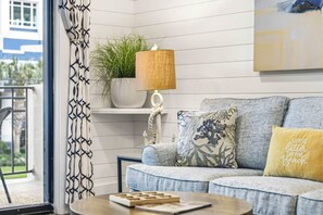 A living room with a sofa, a coffee table, a lamp, a plant, and a window with curtains. - Luxury 2-King Retreat | Heated Pool & Elevator (Myrtle Beach)