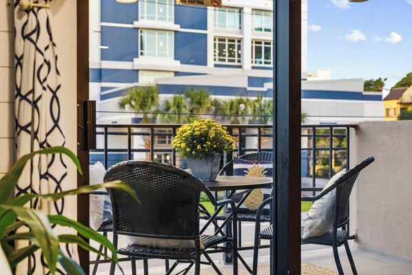 A balcony with outdoor seating, a potted plant, and a view of a building with a 'NO VAPING' sign. - Luxury 2-King Retreat | Heated Pool & Elevator (Myrtle Beach)