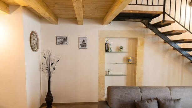 A living room with a grey sofa, a wooden floor, a staircase with a black railing, and a wall with framed pictures and a clock.