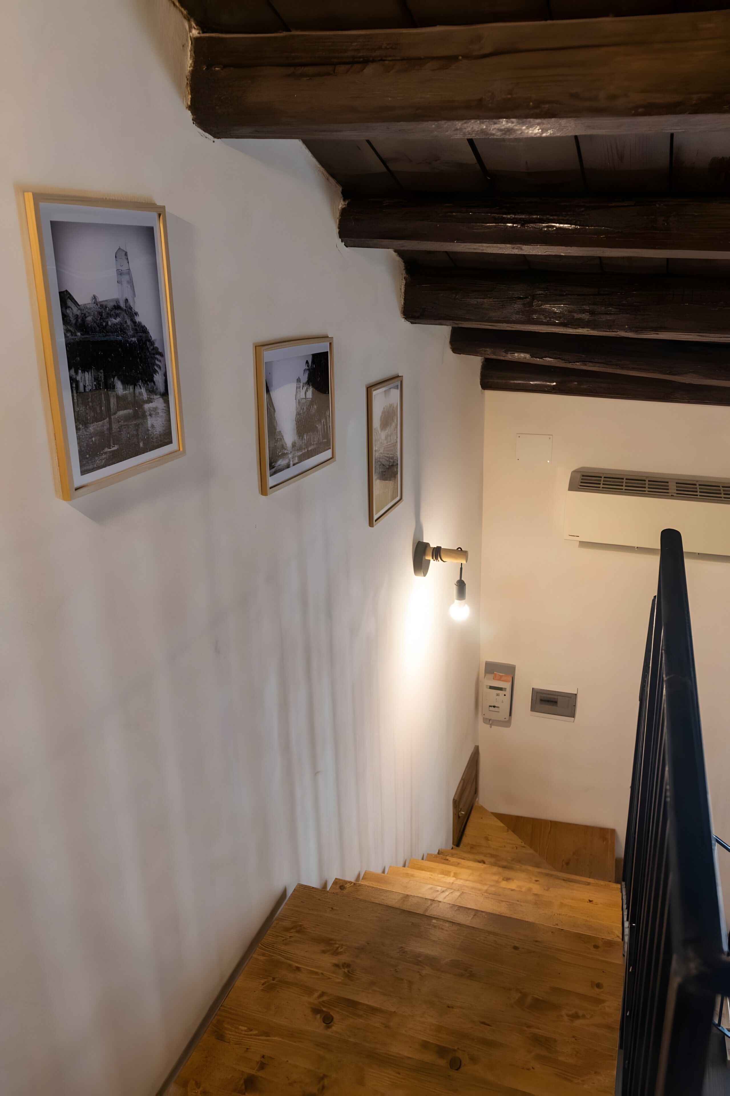 A wooden staircase with white walls and a ceiling with exposed beams. There are three framed pictures on the wall.