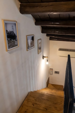 A wooden staircase with white walls and a ceiling with exposed beams. There are three framed pictures on the wall.