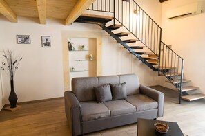 A modern living room with a grey sofa, a wooden coffee table, a black vase, a staircase with black railings, and a white wall with framed pictures.