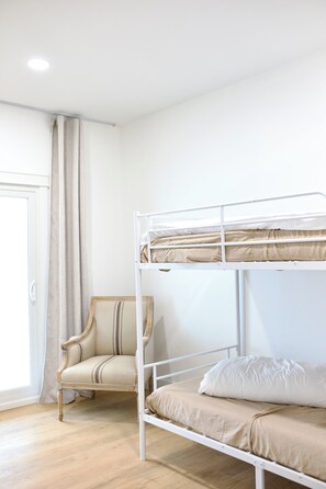 A bunk bed with a chair, wooden floor, and a door with curtains.