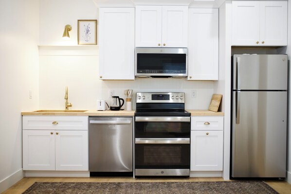 A modern kitchen with white cabinets, stainless steel appliances, and a wooden countertop.