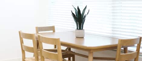 Una mesa redonda de madera para comer con cuatro sillas, una planta en maceta y una ventana con persianas.