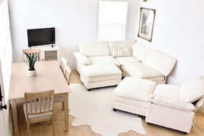 En stue med sofa, skammel, TV og spisebord med stole.
