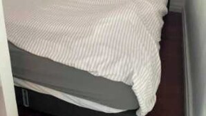 Ein Bett mit dunkelbrauner Kopfteil und weiß gestreifter Bettdecke.