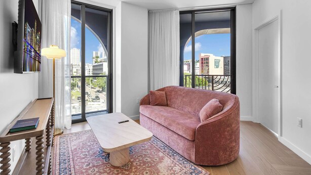 Ein modernes Wohnzimmer mit einer Couch, einem Couchtisch und Blick auf die Stadt durch große Fenster.