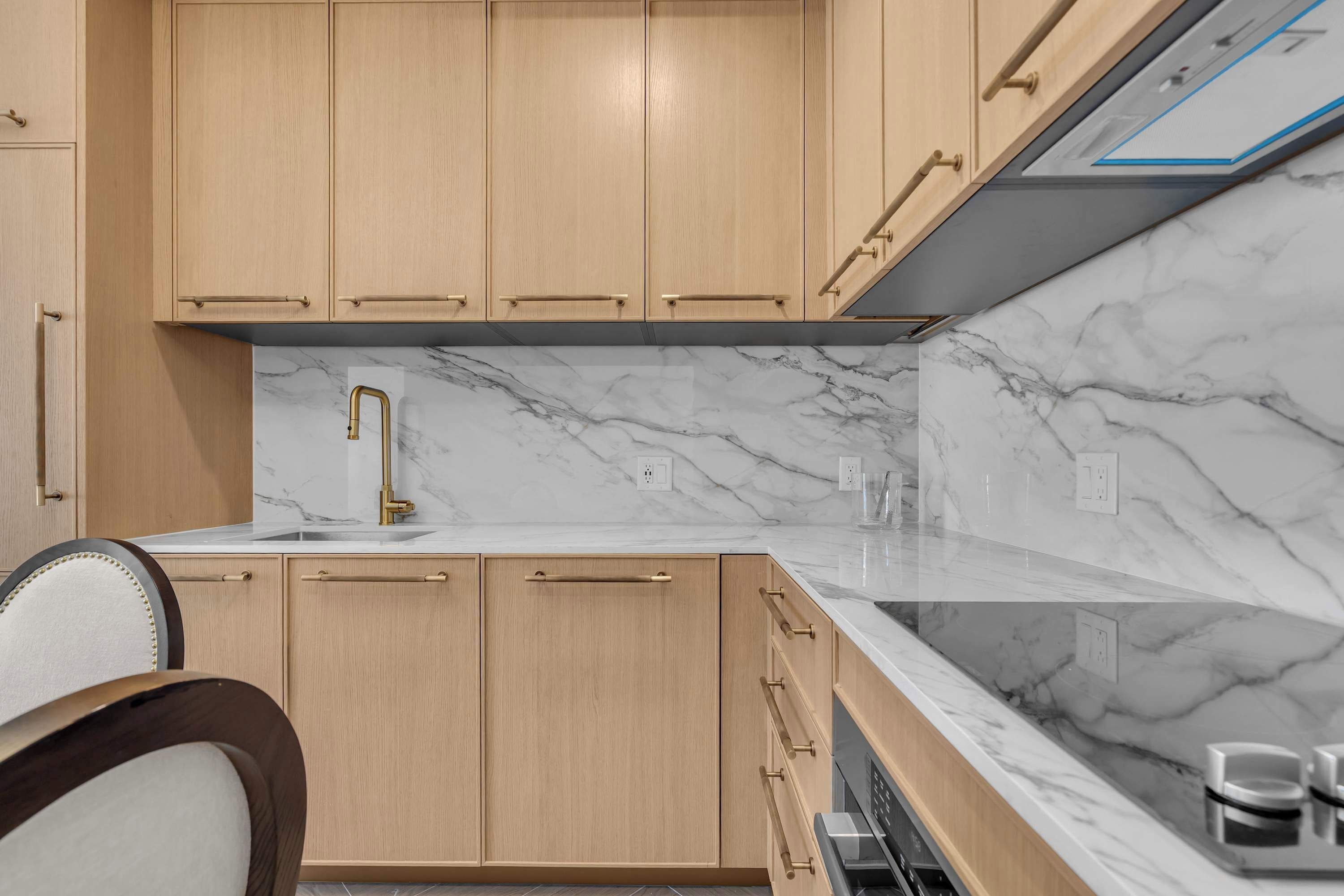 Una cocina moderna con armarios de madera clara, encimera de mármol y campana extractora de acero inoxidable.