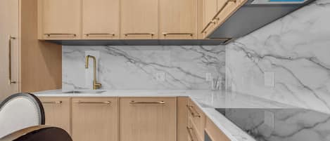 A modern kitchen with light wood cabinetry, a marble countertop, and a stainless steel range hood.