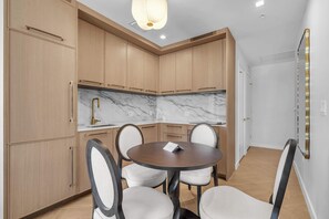 A modern kitchen with wooden cabinets, a marble countertop, and a round dining table with four chairs. - Wynwood Luxury Atelier Resort (Miami)