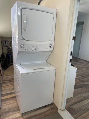 A white front-loading washer and dryer unit with control knobs and a digital display, positioned against a wall with a wooden floor. - Gorgeous 3-bedroom apartment with AC and pool in vibrant Isabela (Isabela)