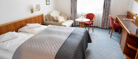 A hotel room with a bed, a desk, a chair, and a sofa.
