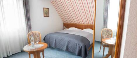 Habitación de hotel con cama, dos sillas, una mesa y un espejo.