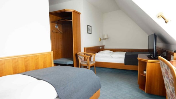 A hotel room with a bed, a desk, a chair, a wardrobe, and a television.