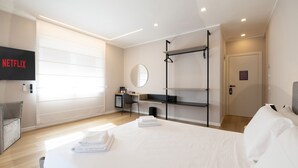 A modern hotel room with a bed, a desk with a computer, a TV, and a wall-mounted shelf. - Lyda Bed&Room (La Spezia)