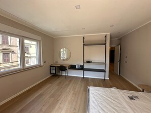 A bedroom with a bunk bed, a desk with a chair, a mirror, and a window with a view of buildings.