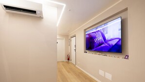 A hallway with a mounted flat-screen TV displaying a purple-themed advertisement, a white air conditioning unit, and a fire extinguisher on the wall. - Lyda Bed&Room (La Spezia)