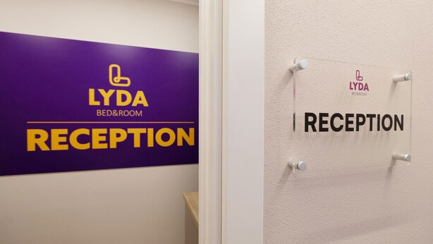 A reception area with a purple sign for LYDA BED&ROOM and a white sign indicating the reception. - Lyda Bed&Room (La Spezia)