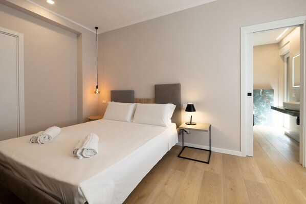 Quarto de hotel com uma cama, uma mesa de cabeceira com abajur e vista para o corredor.